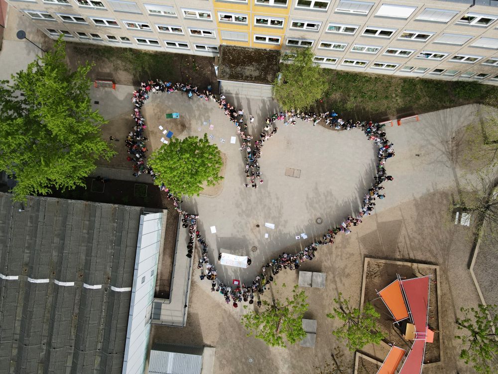 Schülerinnen und Schüler bilden ein Herz auf dem Schulhof
