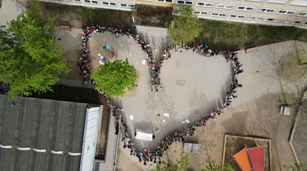 Schülerinnen und Schüler bilden ein Herz auf dem Schulhof